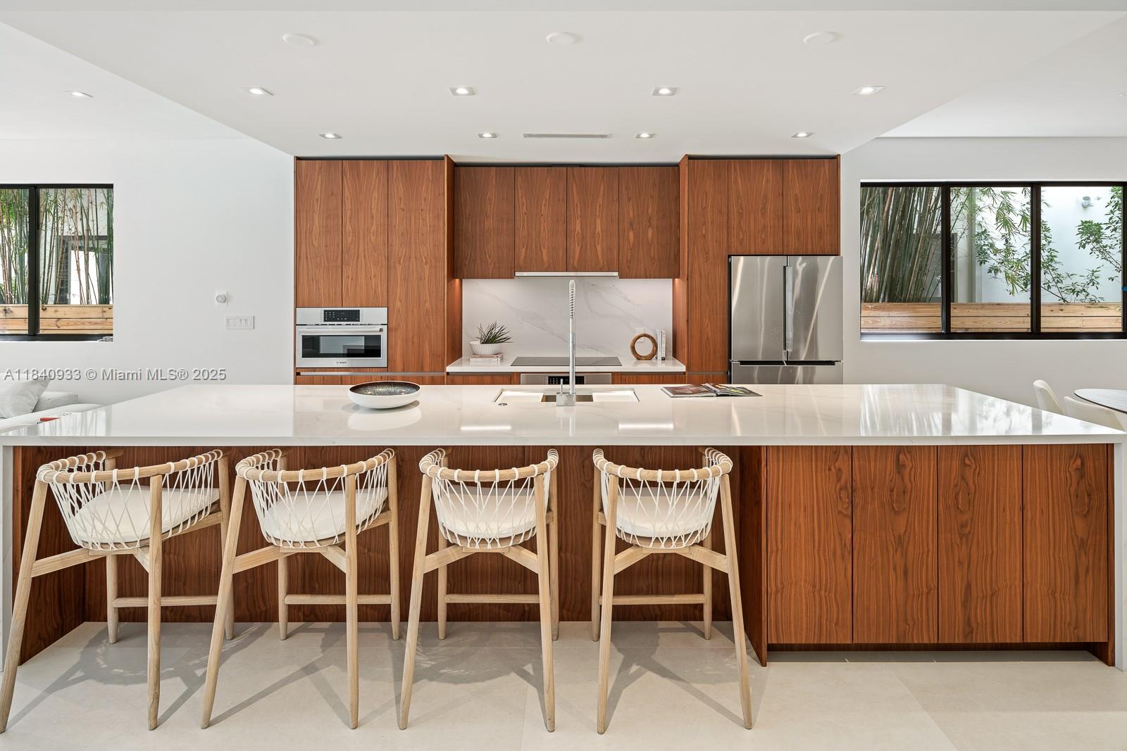 A modern kitchen features wood cabinetry, a white stone island, and four woven bar stools — 2984 Coconut Ave, Coconut Grove FL 33133, COCONUT GROVE, FL