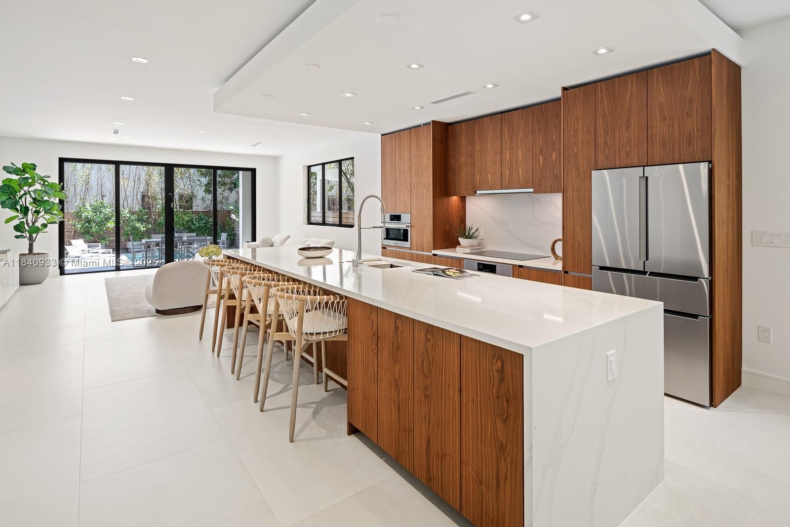 A modern kitchen features wood cabinetry, a large white waterfall island, and sliding glass doors — 2984 Coconut Ave, Coconut Grove FL 33133, COCONUT GROVE, FL