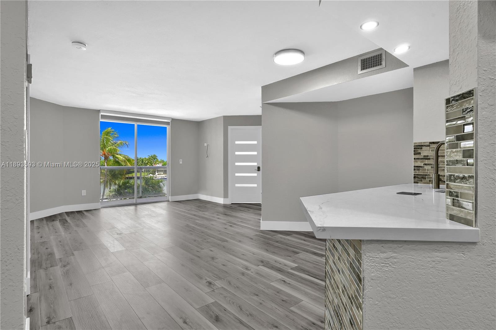 A living area features gray wood-look flooring, a white door, and a kitchen breakfast bar — 5880 Collins Ave # 403, Miami Beach FL 33140, MIAMI BEACH, FL