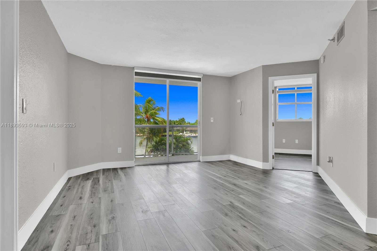 An empty room with gray wood-look flooring, a sliding glass door, and a water view — 5880 Collins Ave # 403, Miami Beach FL 33140, MIAMI BEACH, FL