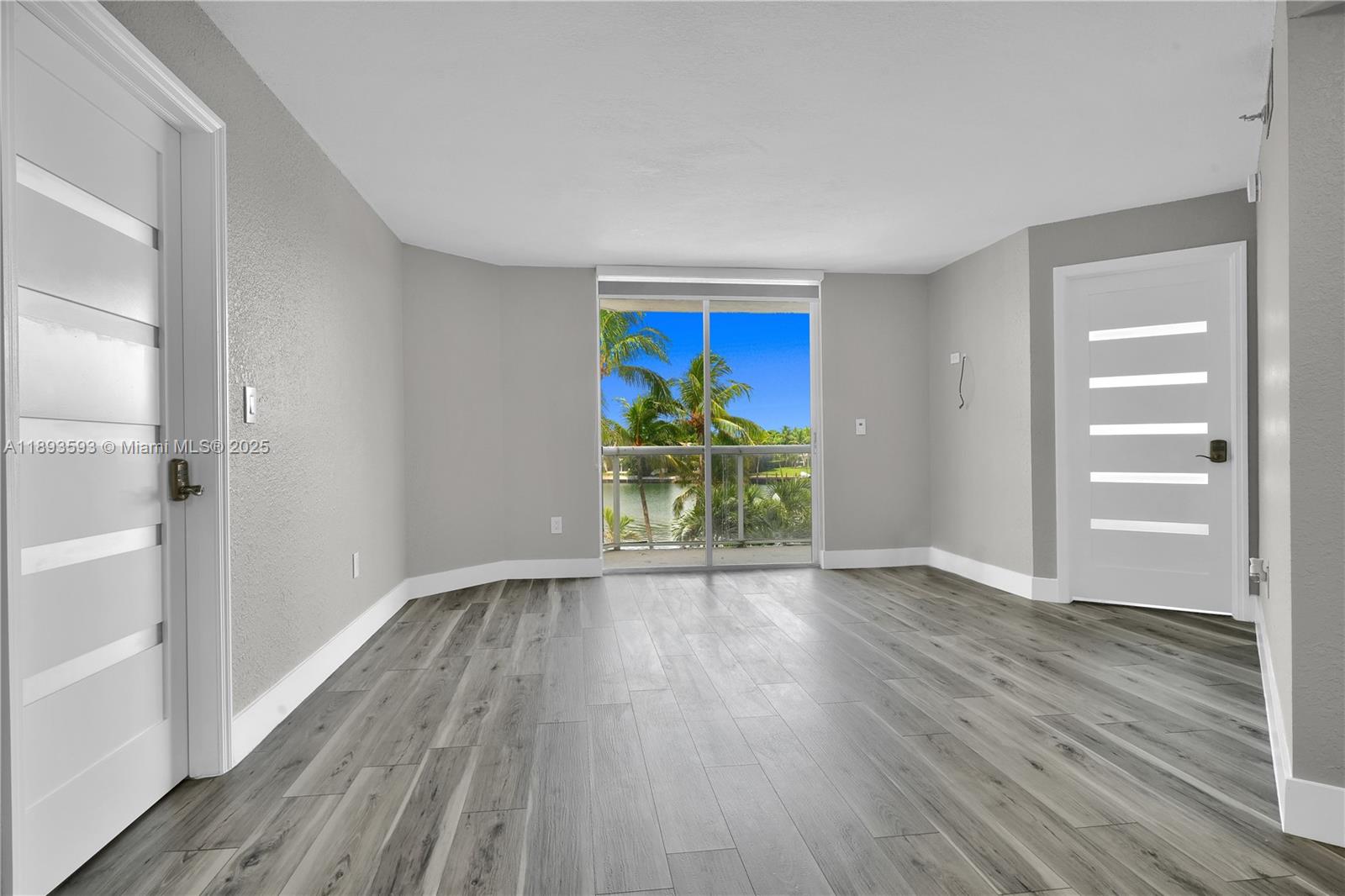 An empty room features gray walls, wood-look flooring, two white doors, and a balcony view — 5880 Collins Ave # 403, Miami Beach FL 33140, MIAMI BEACH, FL
