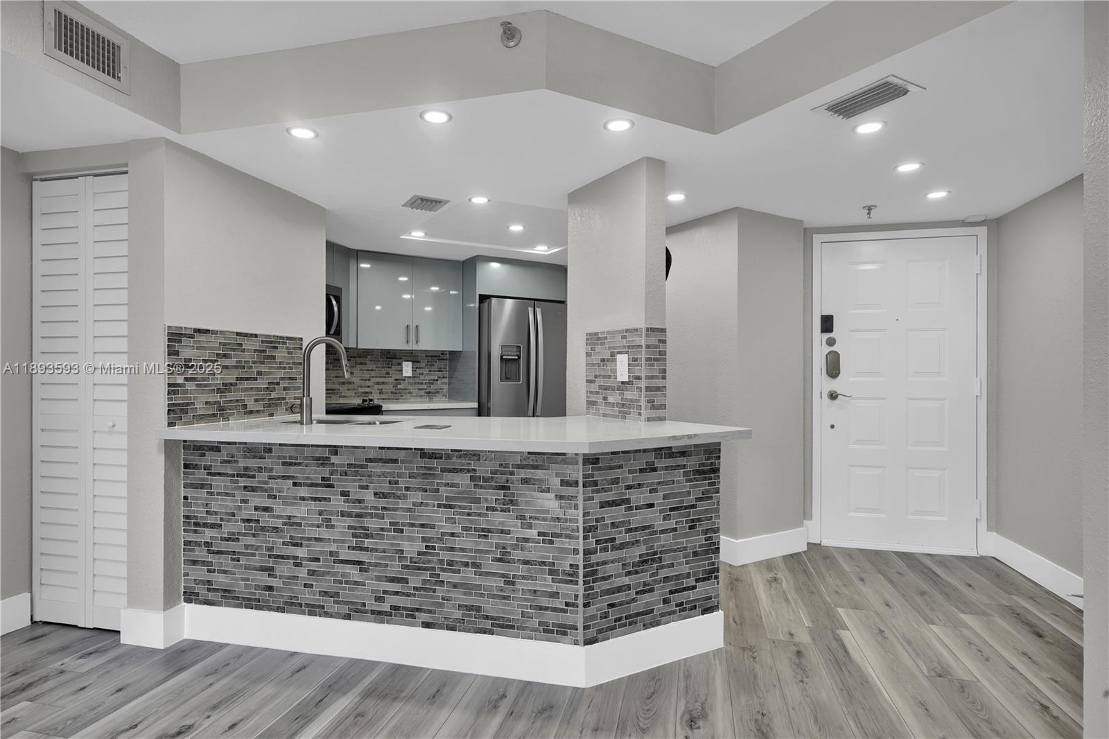 A kitchen features a tiled breakfast bar, gray cabinetry, and light wood-look flooring — 5880 Collins Ave # 403, Miami Beach FL 33140, MIAMI BEACH, FL