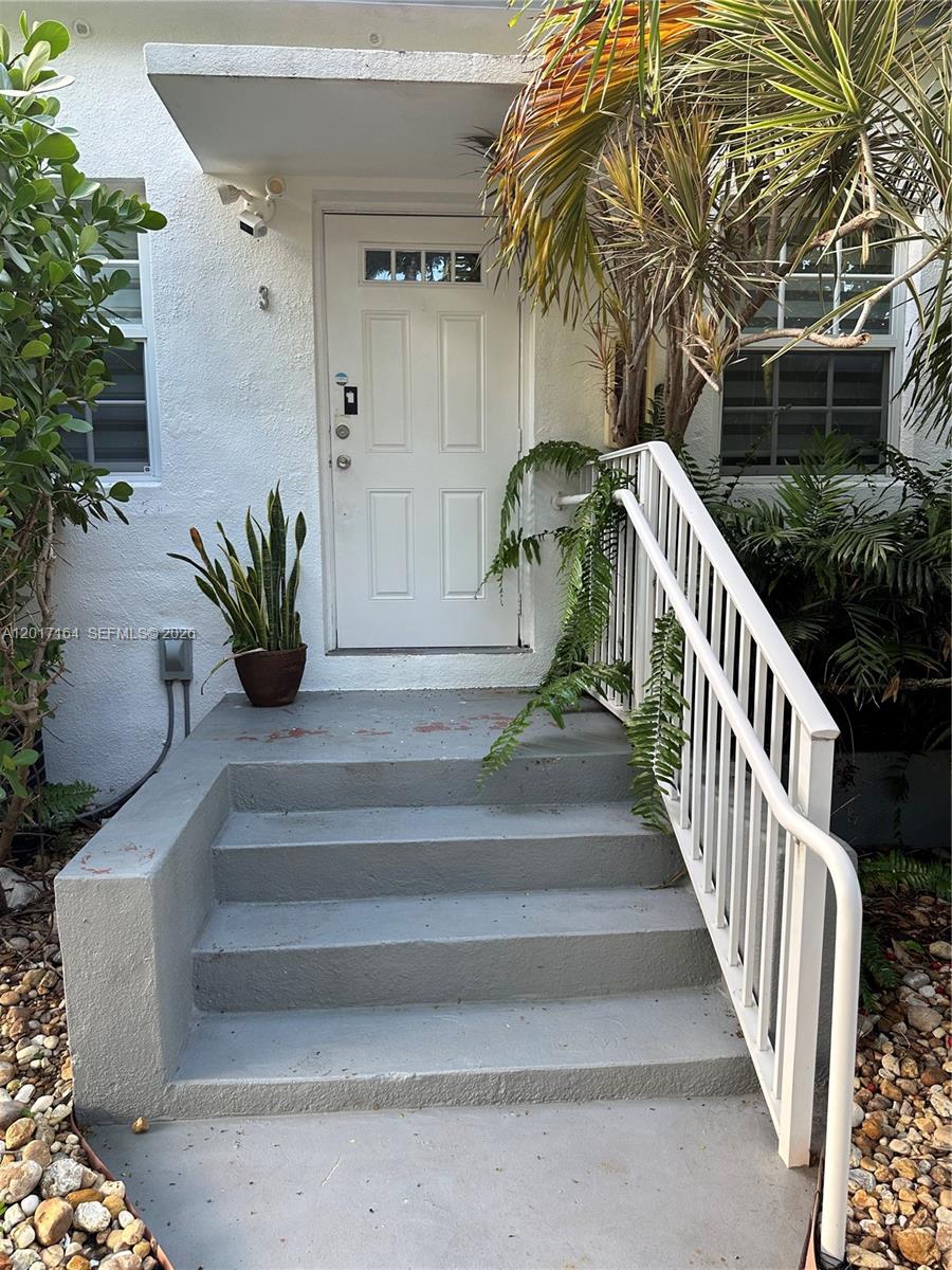 A white front door with a small porch and stairs is surrounded by tropical plants — 8401 Crespi Blvd # 3, Miami Beach FL 33141, MIAMI BEACH, FL