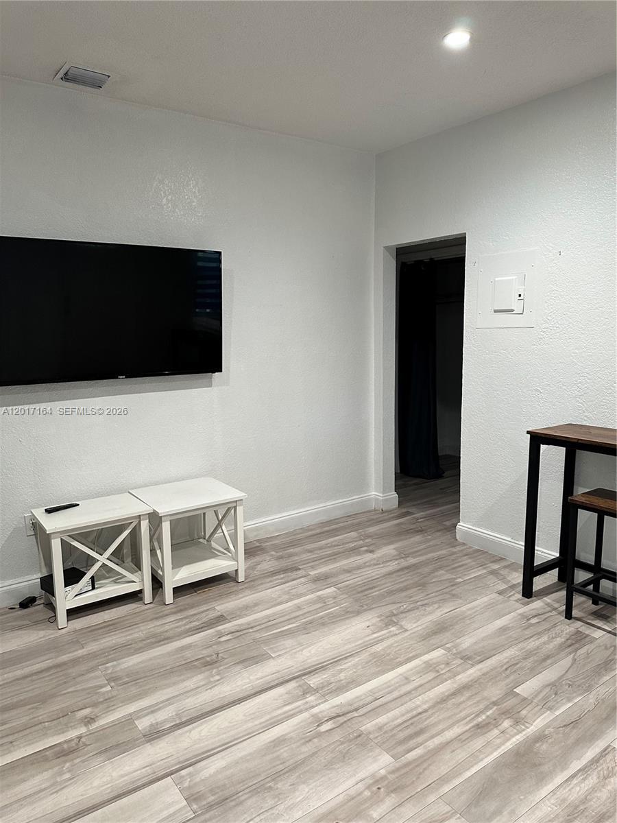 A room features light wood-look flooring, a wall-mounted television, two white side tables, and a doorway — 8401 Crespi Blvd # 3, Miami Beach FL 33141, MIAMI BEACH, FL