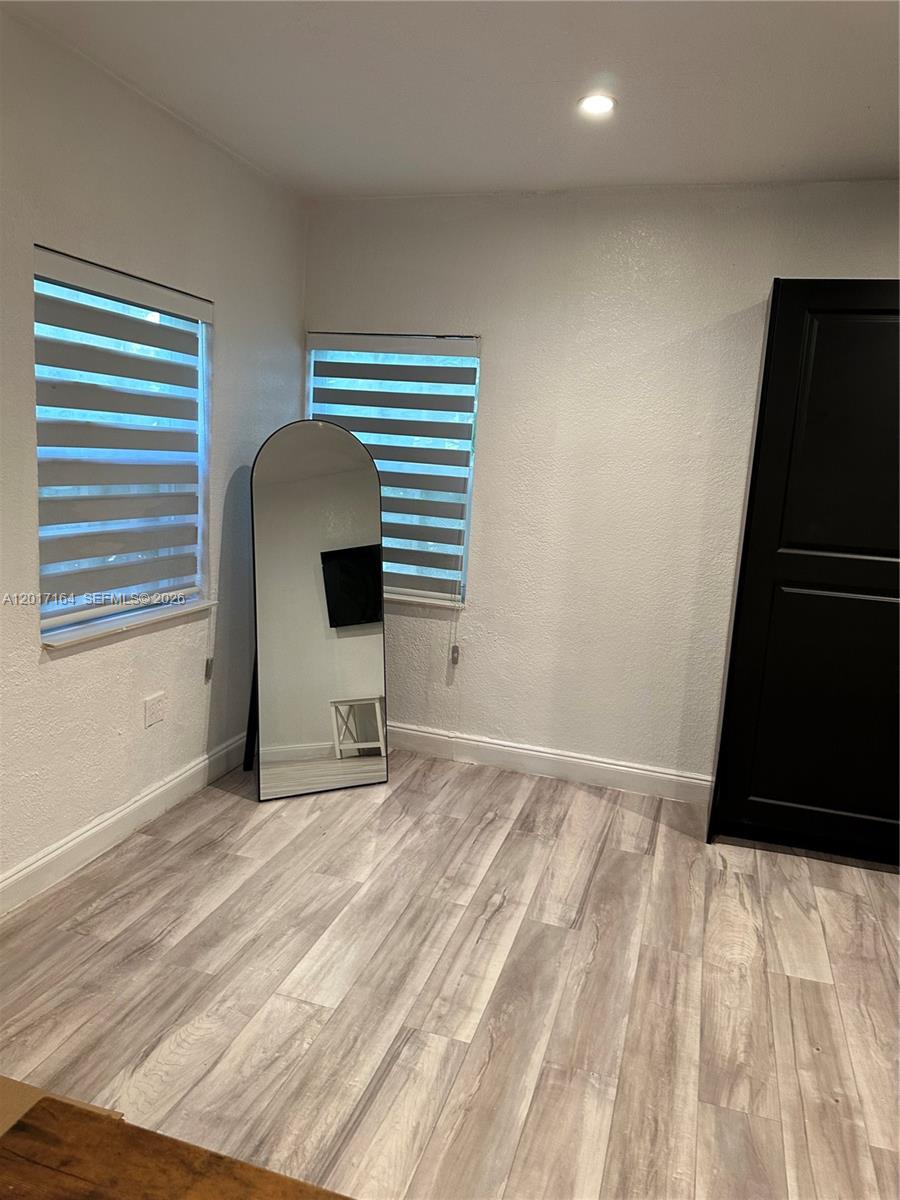 A room with light wood-look flooring, two windows with striped shades, and a floor mirror — 8401 Crespi Blvd # 3, Miami Beach FL 33141, MIAMI BEACH, FL