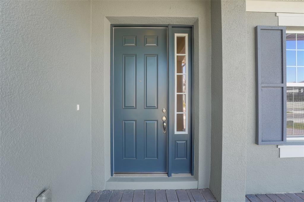 A blue front door with a side light window is set in a gray exterior wall — 14371 CREST PALM AVENUE, WINDERMERE, FL
