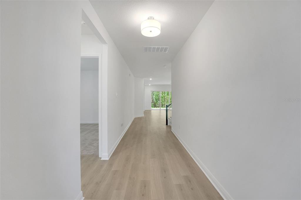 A bright hallway with light wood-look flooring leads toward a glass sliding door — 14371 CREST PALM AVENUE, WINDERMERE, FL