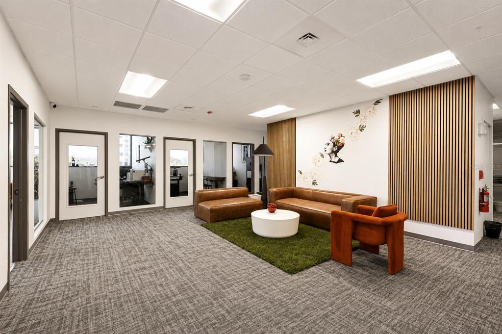 A modern office lounge features a leather sofa, armchair, green rug, and a mural wall — 3707 W CHERRY STREET, TAMPA, FL