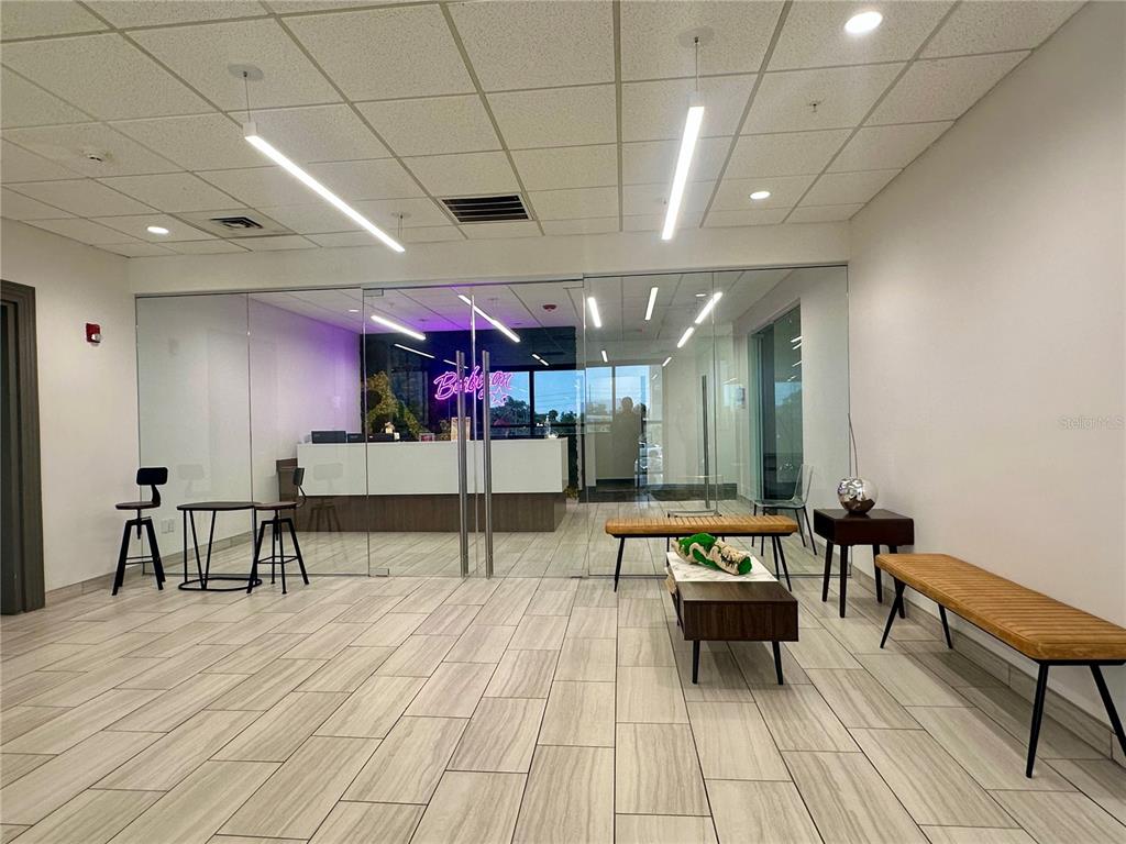 A modern office lobby features glass walls, wood-look tile flooring, and a reception desk area — 3707 W CHERRY STREET, TAMPA, FL