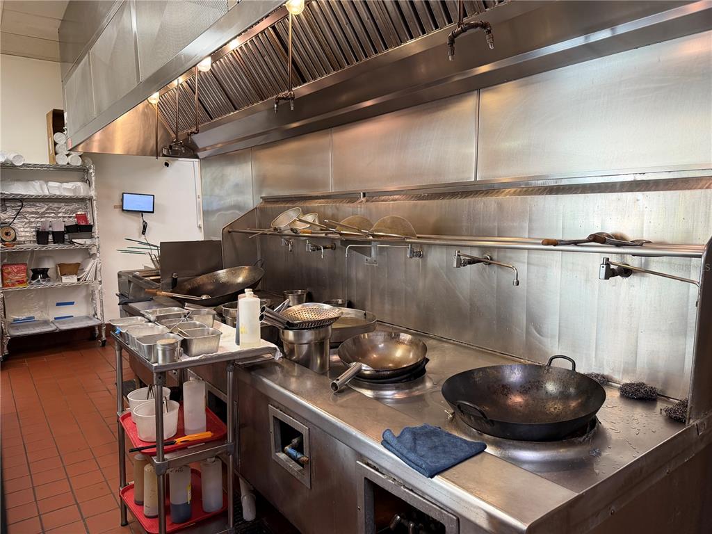 A commercial kitchen features stainless steel counters, a large exhaust hood, and several woks — 12141 S ORANGE BLOSSOM TRAIL, ORLANDO, FL