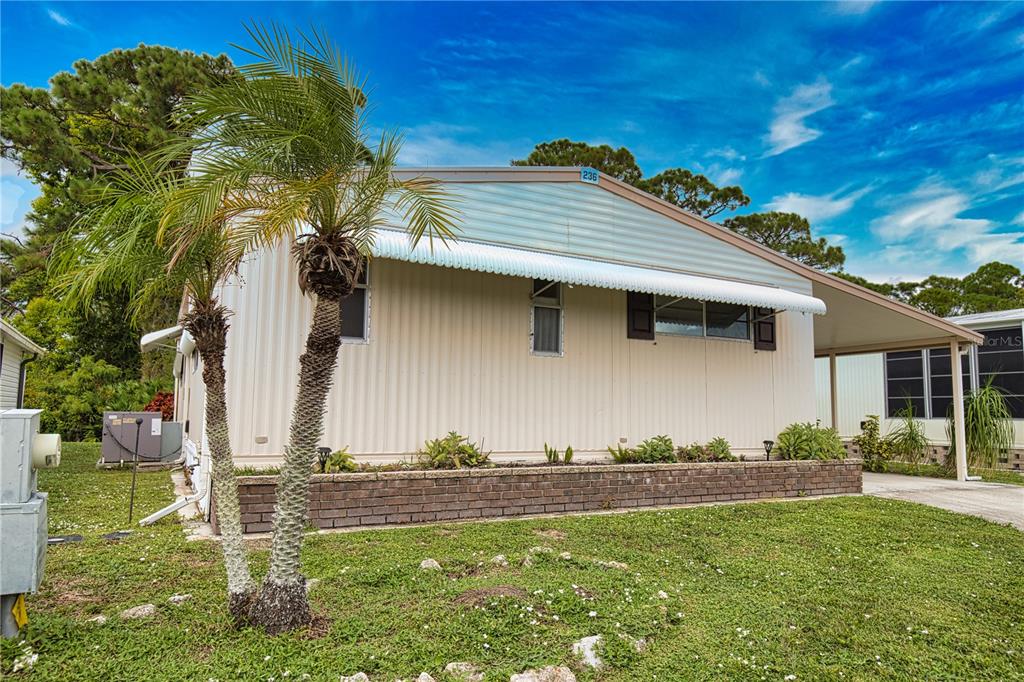 A single-story mobile home with light siding, a brick planter, and a palm tree — 236 N FIJI CIRCLE, ENGLEWOOD, FL