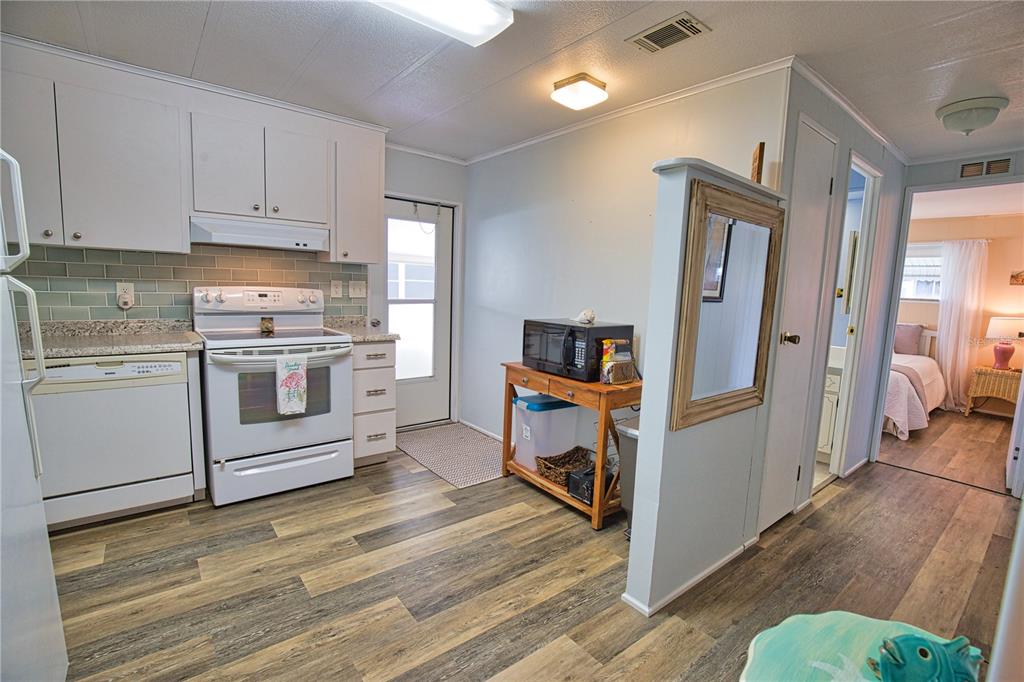 A kitchen with white cabinets, a white stove, and wood-look flooring leads to a bedroom — 236 N FIJI CIRCLE, ENGLEWOOD, FL