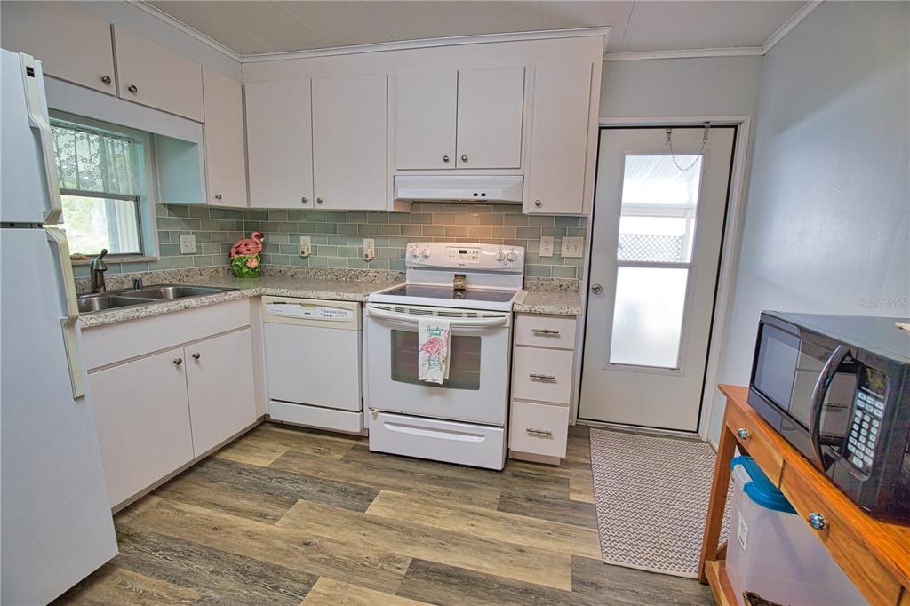 A kitchen features white cabinets, a light green subway tile backsplash, and wood-look flooring — 236 N FIJI CIRCLE, ENGLEWOOD, FL