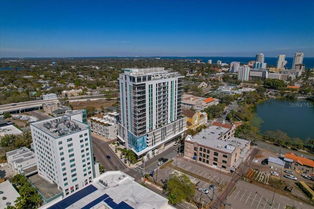 An aerial view shows a tall modern apartment building surrounded by city streets and a lake — 777 3RD AVENUE N UNIT 1202, ST PETERSBURG, FL