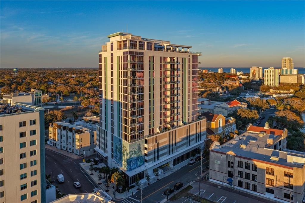 An aerial view of a tall, modern apartment building featuring a large mural on its side — 777 3RD AVENUE N UNIT 1202, ST PETERSBURG, FL