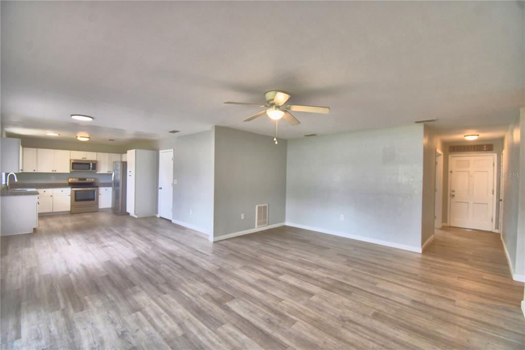 An open-concept living area with light wood-look flooring, a ceiling fan, and an adjacent kitchen — 105 BYRON PLACE, WINTER HAVEN, FL