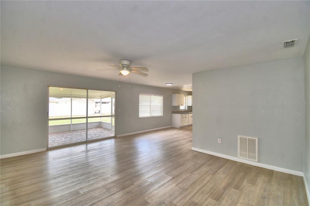 An open-concept living area features light wood-look flooring, a ceiling fan, and a sliding glass door — 105 BYRON PLACE, WINTER HAVEN, FL