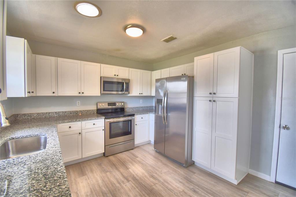 A kitchen features white cabinets, stainless steel appliances, granite countertops, and light wood-look flooring — 105 BYRON PLACE, WINTER HAVEN, FL