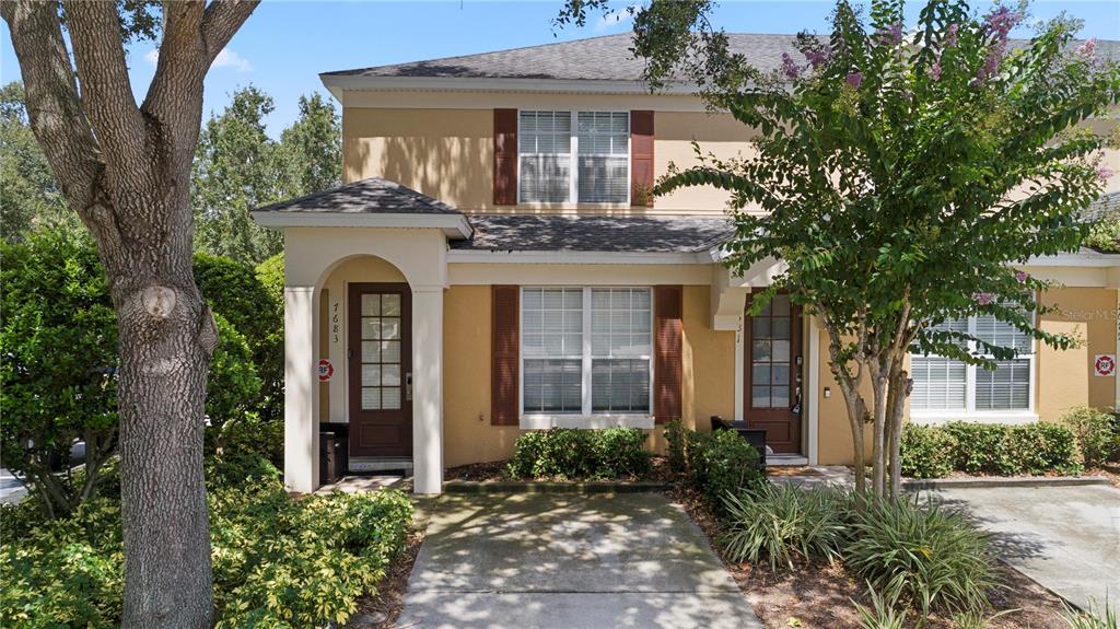 A two-story townhouse exterior with tan stucco walls, brown shutters, and a concrete walkway — 7683 FITZCLARENCE STREET, KISSIMMEE, FL