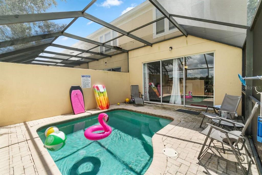 A screened-in patio features a small swimming pool, patio furniture, and various pool floats — 7683 FITZCLARENCE STREET, KISSIMMEE, FL