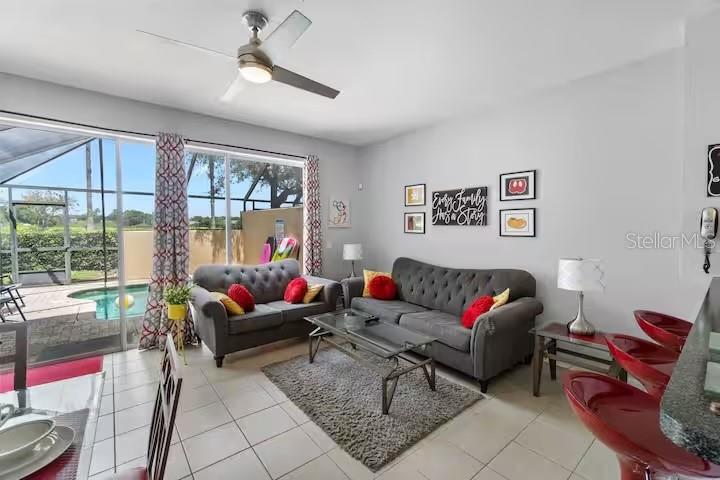 A living room features two grey sofas, a glass coffee table, and a sliding door — 7683 FITZCLARENCE STREET, KISSIMMEE, FL
