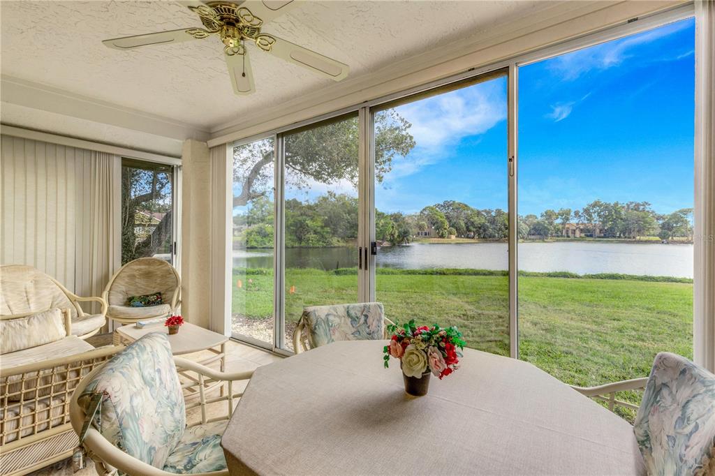 A sunroom with a dining table and wicker chairs overlooks a lake through sliding glass doors — 3242 RINGWOOD MEADOW UNIT 76, SARASOTA, FL