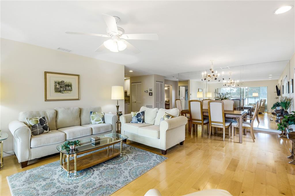 A living room and dining area feature light-colored sofas, a glass coffee table, and hardwood floors — 3242 RINGWOOD MEADOW UNIT 76, SARASOTA, FL