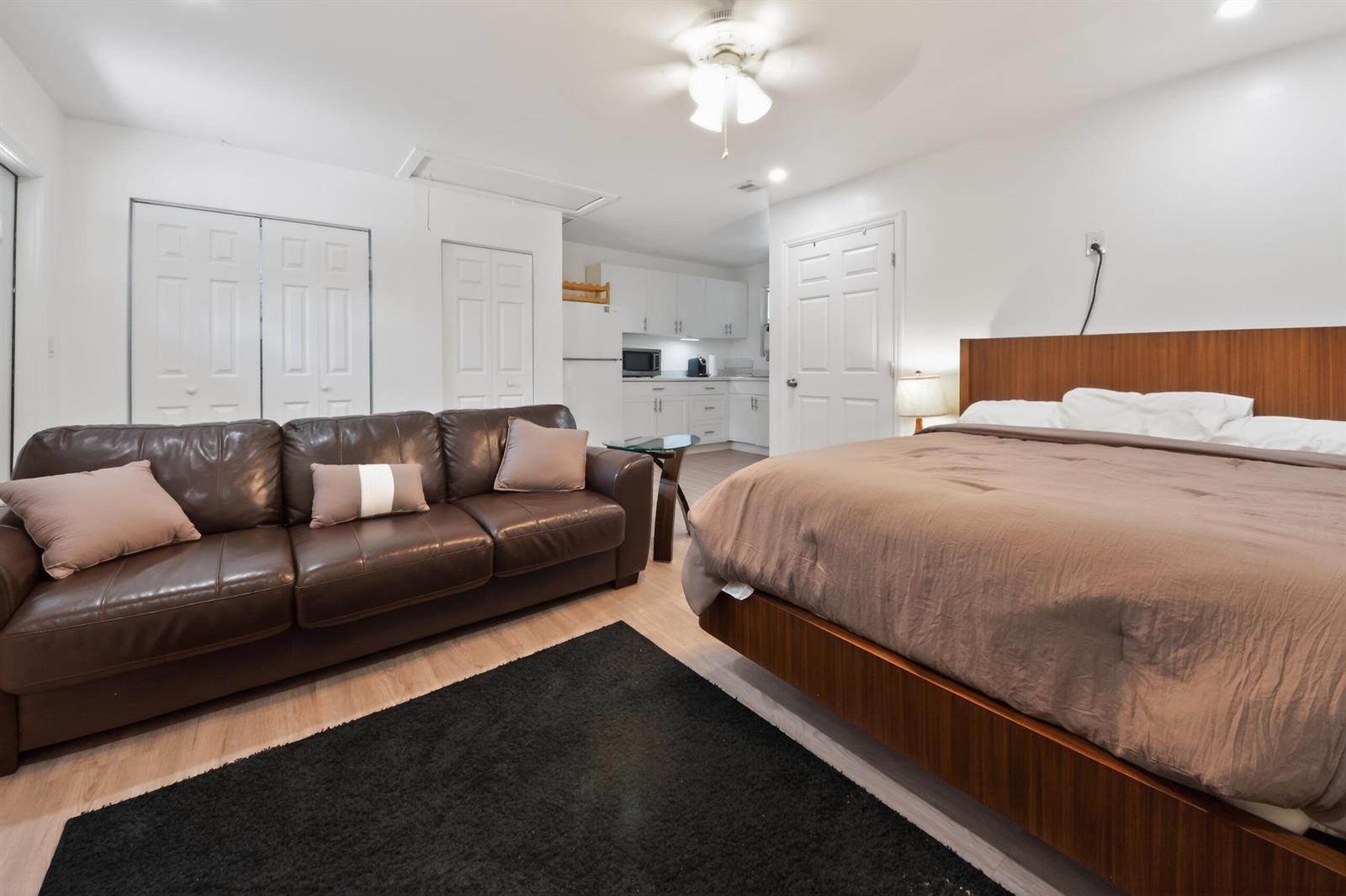 A studio apartment features a bed, a brown leather sofa, and a small kitchen area — 10754 Tamis Trail Unit B, Lake Worth FL 33449, LAKE WORTH, FL