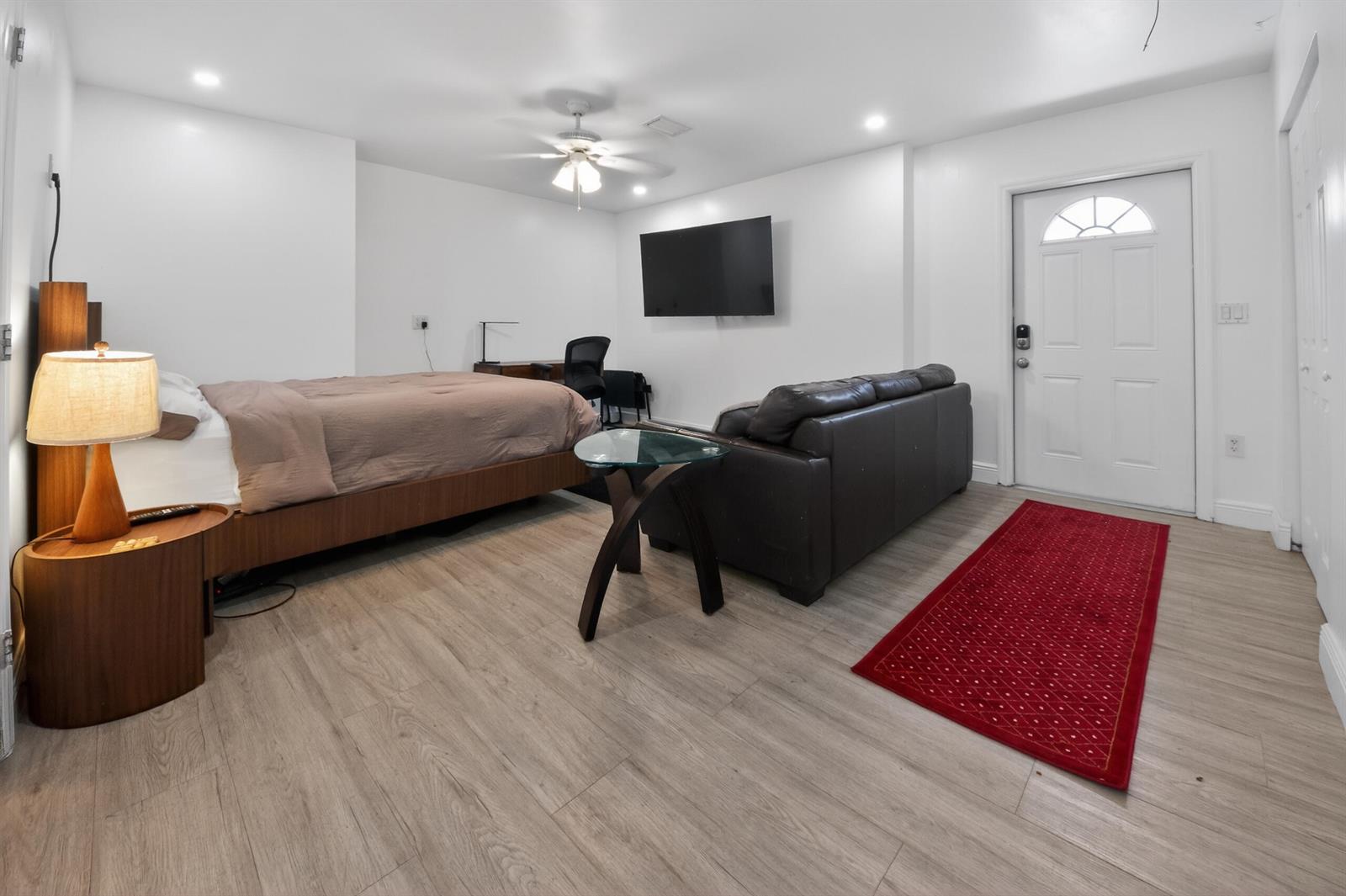 A studio apartment features a bed, sofa, desk, wall-mounted television, and a red entry rug — 10754 Tamis Trail Unit B, Lake Worth FL 33449, LAKE WORTH, FL