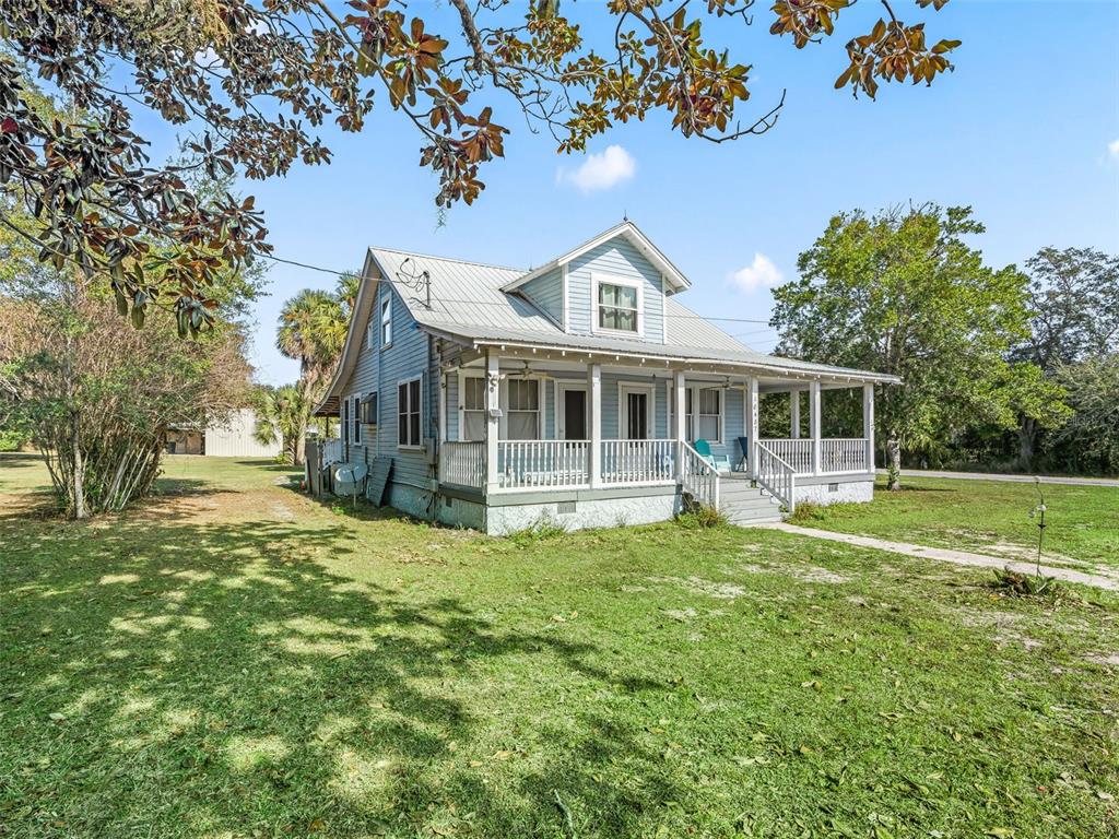 A light blue house with a metal roof and a wrap-around porch sits on grass — 10487 SE HIGHWAY 42, SUMMERFIELD, FL