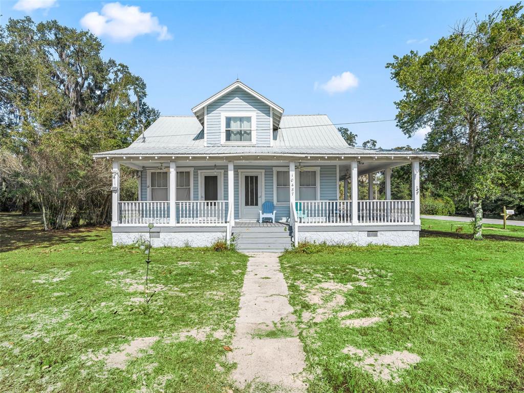 A light blue, two-story farmhouse features a wraparound porch and a metal roof — 10487 SE HIGHWAY 42, SUMMERFIELD, FL