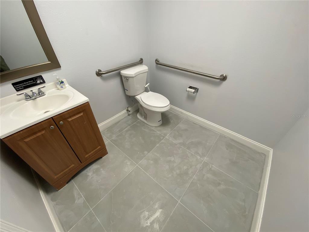 A bathroom features a wood vanity, a toilet with grab bars, and gray tile flooring — 1004 PLAZA DRIVE UNIT 105, KISSIMMEE, FL