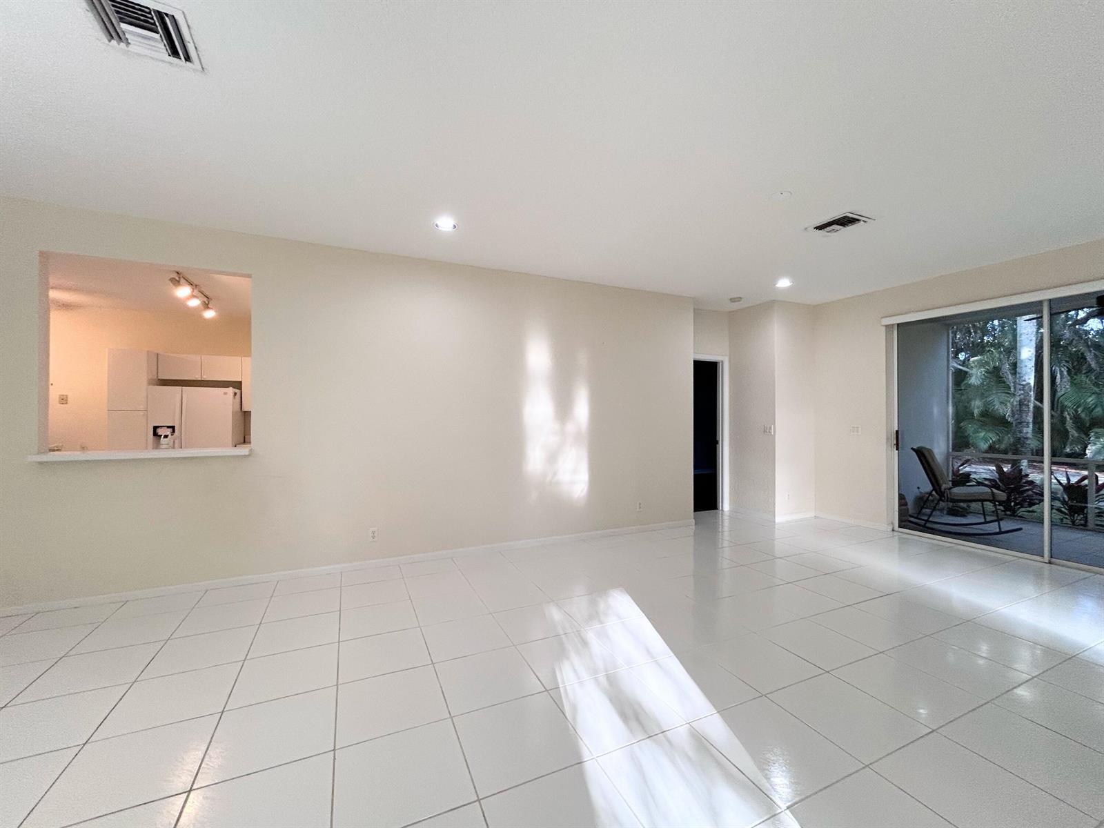 An empty living room with white tile floors, a kitchen pass-through, and sliding glass doors — 7910 Laina Lane # 2, Boynton Beach FL 33437, BOYNTON BEACH, FL