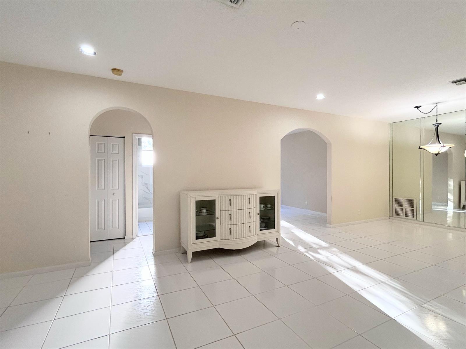 A bright, tiled room features two arched doorways, a white sideboard, and mirrored wall panels — 7910 Laina Lane # 2, Boynton Beach FL 33437, BOYNTON BEACH, FL