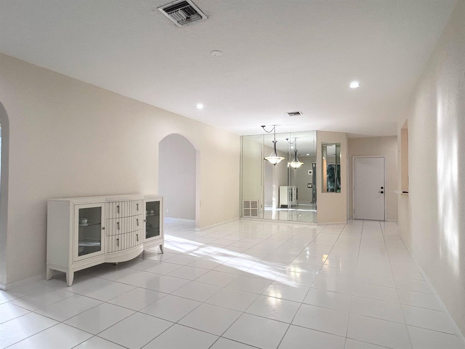 A bright, empty room features white tile flooring, a mirrored wall, and a white sideboard — 7910 Laina Lane # 2, Boynton Beach FL 33437, BOYNTON BEACH, FL