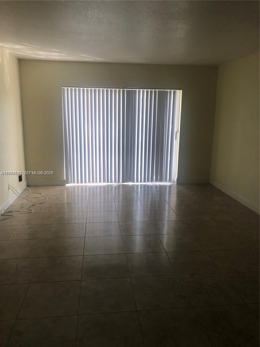 An empty room features light-colored tile flooring, beige walls, and a large sliding glass door — 2834 NW 55th Ave # 1C, Lauderhill FL 33313, LAUDERHILL, FL