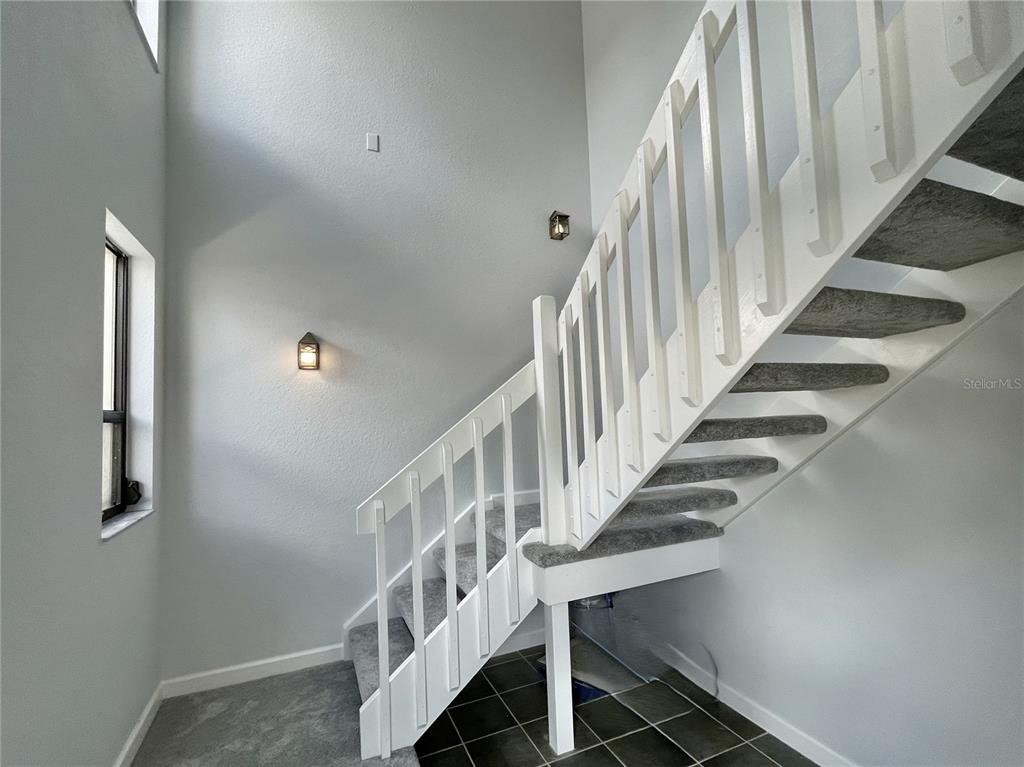 A staircase with white railings and gray carpet leads upward in a high-ceilinged entryway — 1335 SAXONY CIRCLE UNIT 322, PUNTA GORDA, FL
