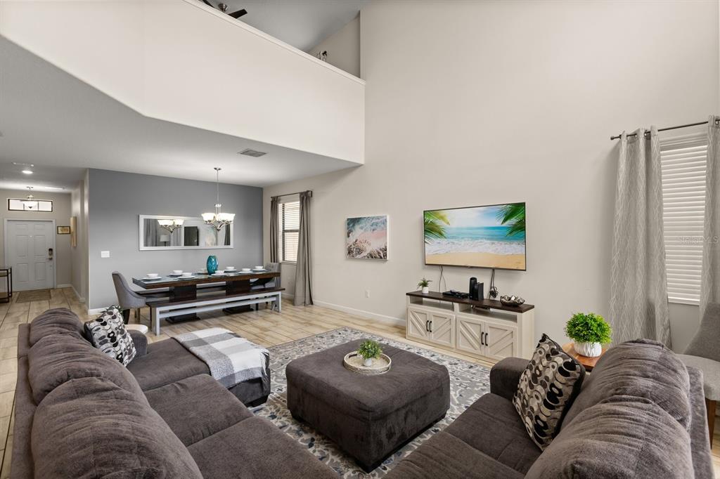 A living room with a sectional sofa, ottoman, dining area, and high ceilings — 5493 SOLTERRA CIRCLE, DAVENPORT, FL