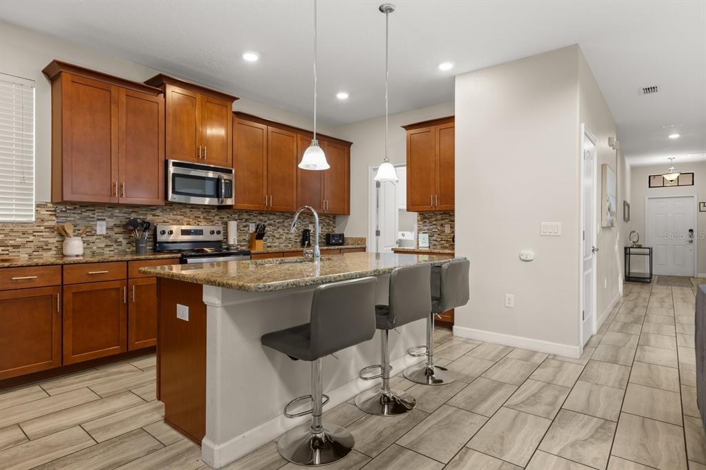 A kitchen with wood cabinets, granite countertops, a center island with stools, and tile flooring — 5493 SOLTERRA CIRCLE, DAVENPORT, FL