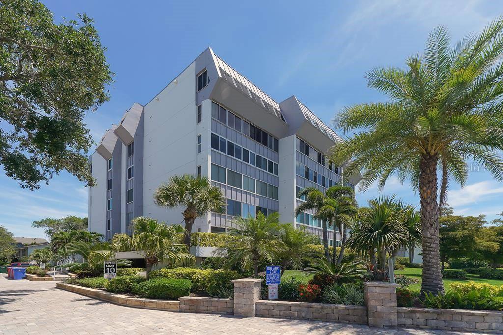 A multi-story apartment building with a gray facade is surrounded by palm trees and landscaping — 1200 E PEPPERTREE LANE UNIT 206, SARASOTA, FL