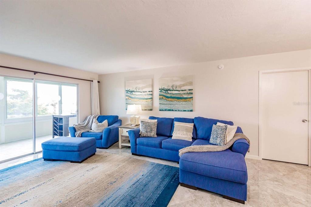 A living room features blue furniture, a large area rug, and sliding glass doors — 1200 E PEPPERTREE LANE UNIT 206, SARASOTA, FL