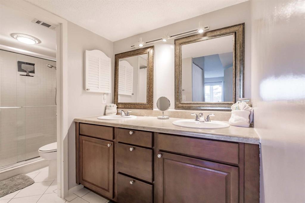 A bathroom features a double vanity with dark wood cabinets, beige countertops, and two mirrors — 1200 E PEPPERTREE LANE UNIT 206, SARASOTA, FL