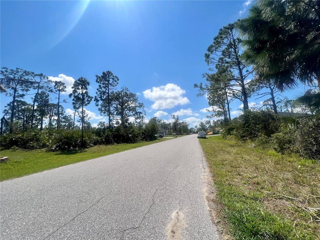 A paved road stretches through a wooded residential area under a bright blue sky — 5327 VENUS TERRACE, PORT CHARLOTTE, FL