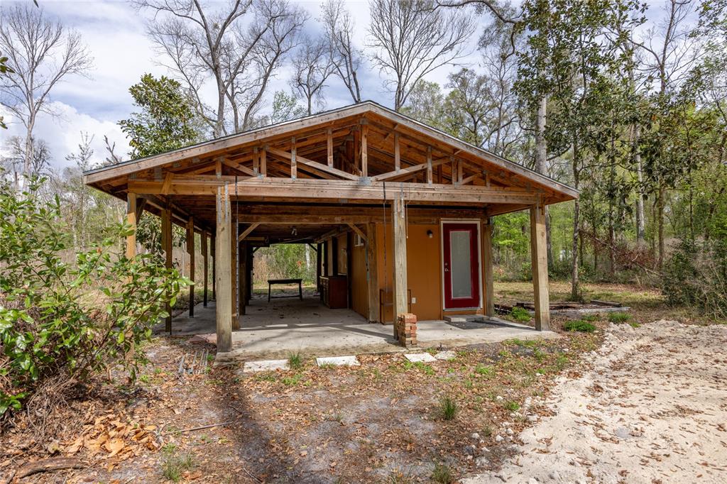 An outdoor covered patio with a concrete floor, wooden support beams, and a red door — 1187 SW BOSTON TERRACE, FORT WHITE, FL