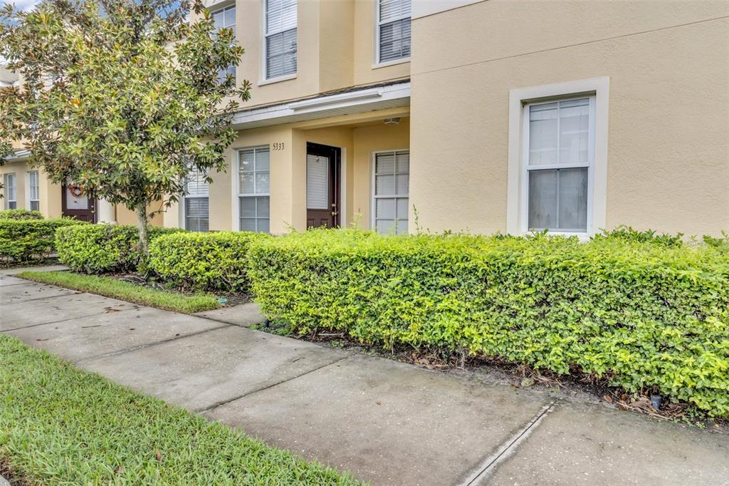 A tan two-story townhouse exterior with a sidewalk, manicured hedges, and a front entrance — 5333 RIVER ROCK ROAD, LAKELAND, FL
