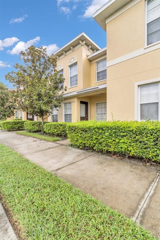 The exterior of a two-story tan townhouse features a sidewalk and manicured green hedges — 5333 RIVER ROCK ROAD, LAKELAND, FL