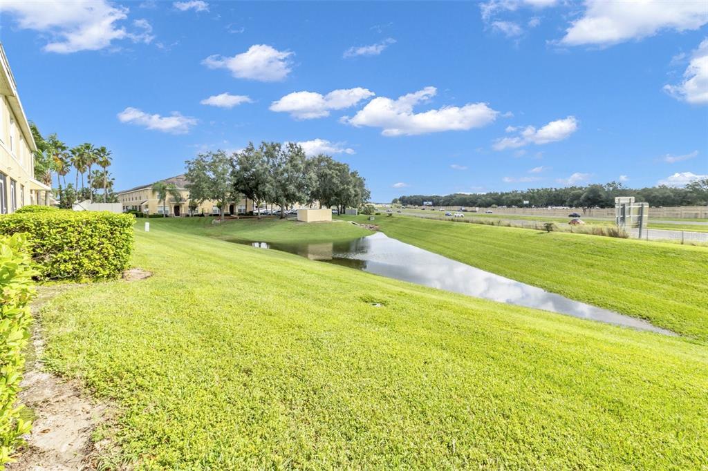A grassy lawn slopes down toward a small retention pond behind a multi-story apartment building — 5333 RIVER ROCK ROAD, LAKELAND, FL