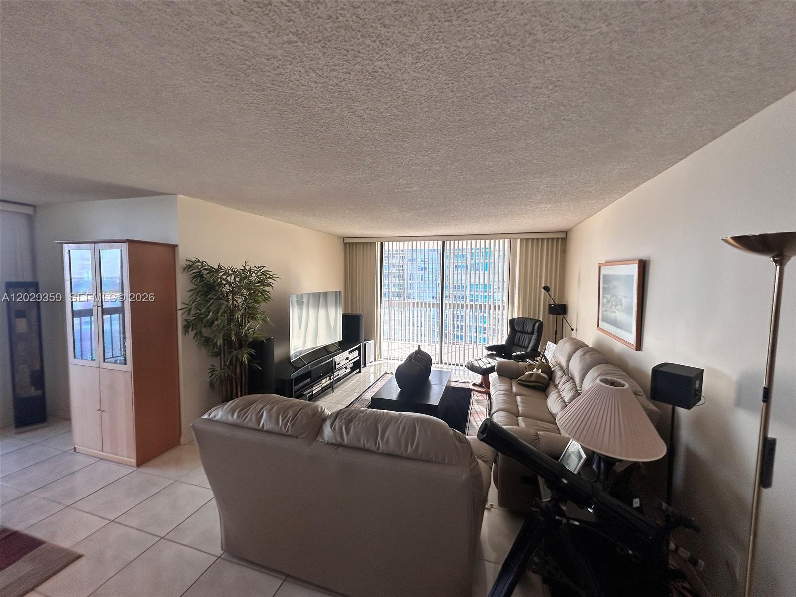A living room features light-colored tile floors, a beige sofa set, and a large window — 2333 Brickell Ave # 1402, Miami FL 33129, MIAMI, FL