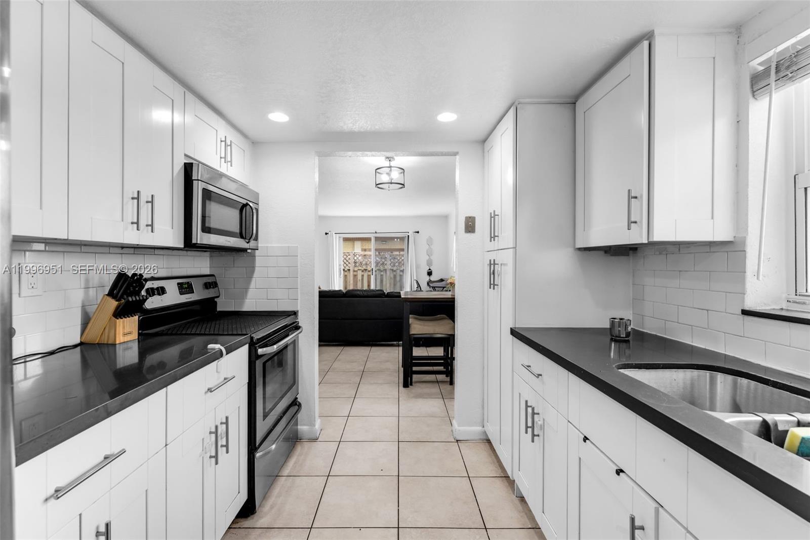 A galley kitchen features white cabinets, black countertops, and stainless steel appliances — 8500 SW 109th Ave # 114, Miami FL 33173, MIAMI, FL