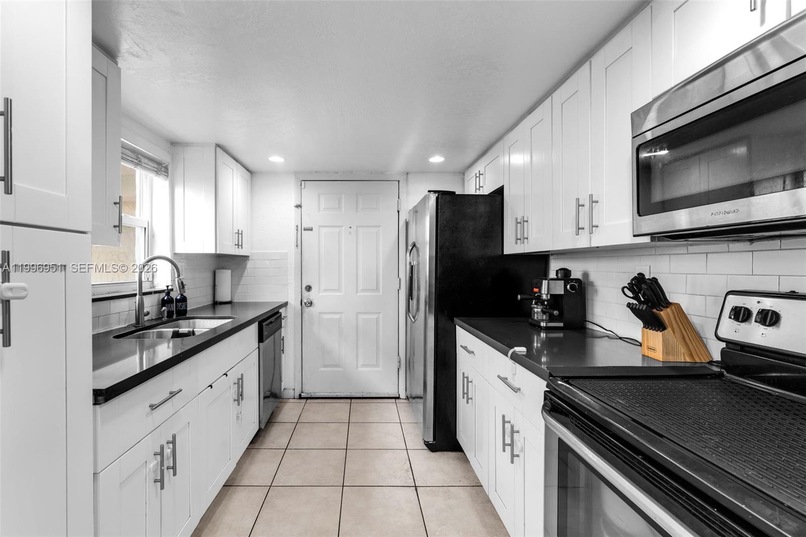 A galley kitchen features white cabinets, black countertops, stainless steel appliances, and tile flooring — 8500 SW 109th Ave # 114, Miami FL 33173, MIAMI, FL